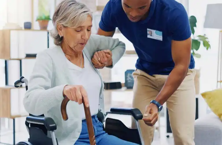 A live-in home health aide helps their patient to stand in Owings Mills, MD